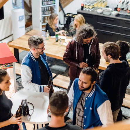 Mitarbeiter mit blauen Bleech Jacken und Besucher:innen unterhalten sich in gelassener Atmosphäre stehend im Office.